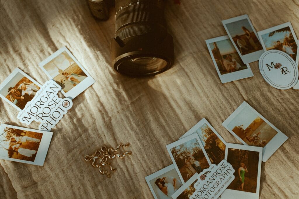 A warm, nostalgic, flatlay of polaroids, Morgan Rose Photography Stickers, gold bow earrings, and a camera lens arranged on a textured blanket.