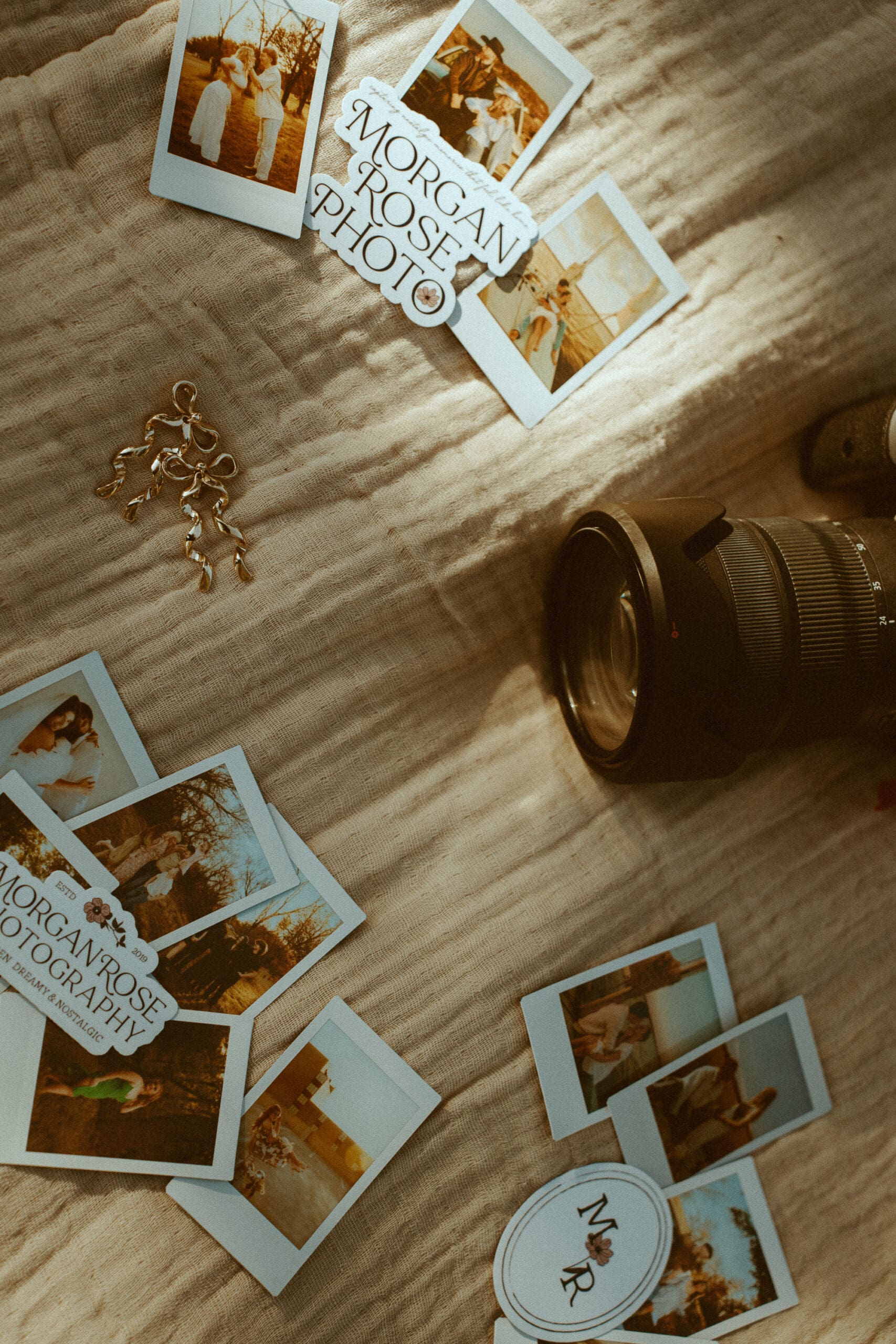 A warm, nostalgic, flatlay of polaroids, Morgan Rose Photography Stickers, gold bow earrings, and a camera lens arranged on a textured blanket.