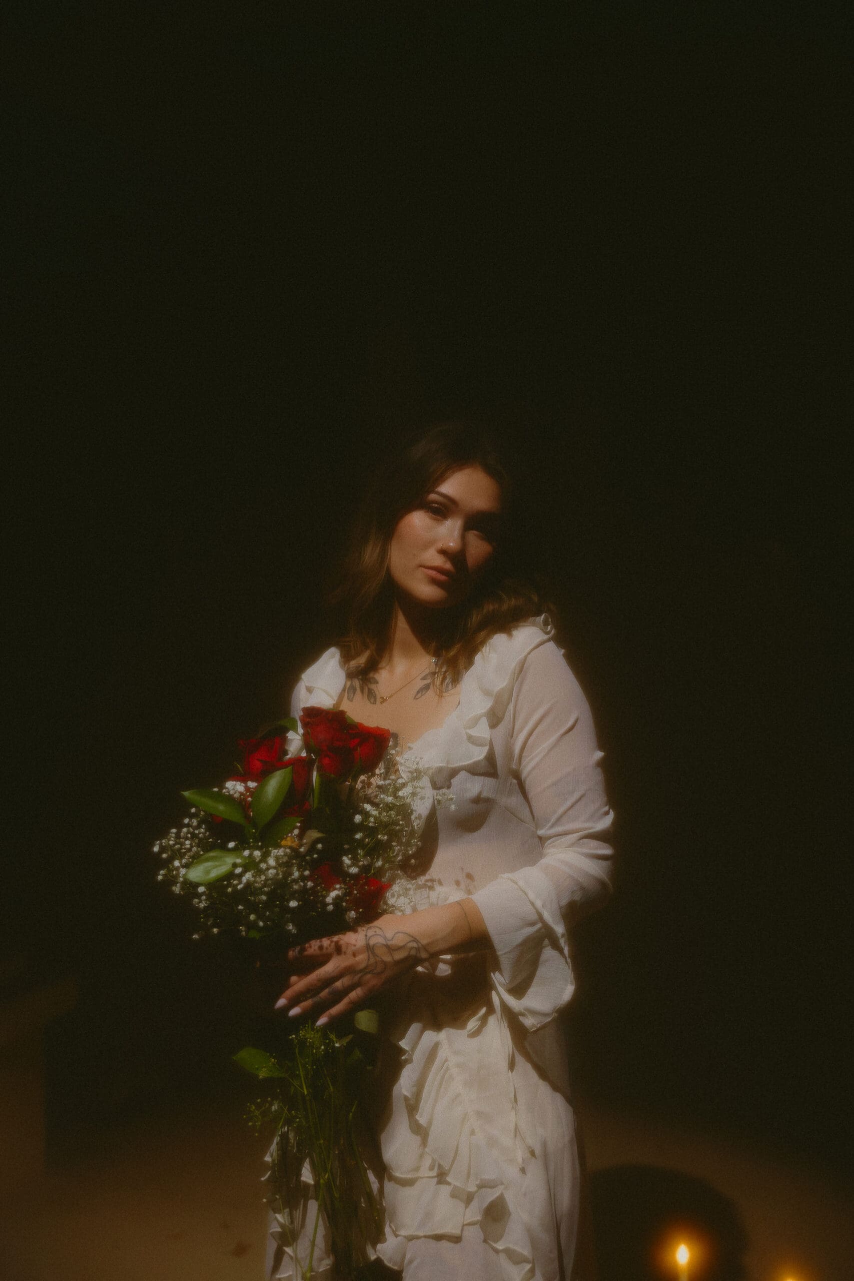 Cinematic portrait of a woman holding a bouquet of red roses in soft, dramatic lighting. Moody lifestyle photography with warm tones, nostalgic styling, and editorial-inspired shadows. Perfect example of creative portrait photography, fine art portraits, and golden-hour-inspired indoor lighting. Ideal for photographers showcasing emotional, artistic, storytelling portrait work.