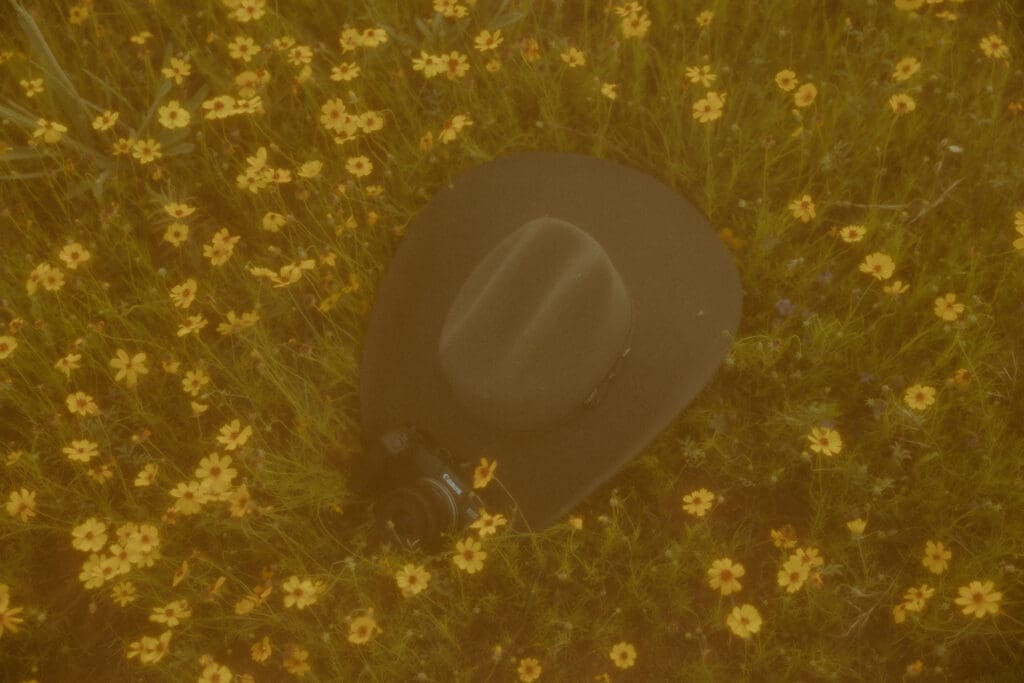 Western themed branding detail image with cowboy hat and camera in yellow flower field in Abilene, TX
