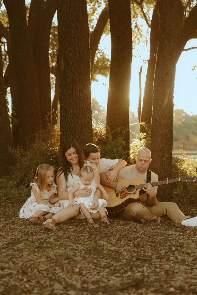 Family wearing neutral outfits that photograph beautifully during a golden hour fall family photo session in a field by trees in Abilene, TX