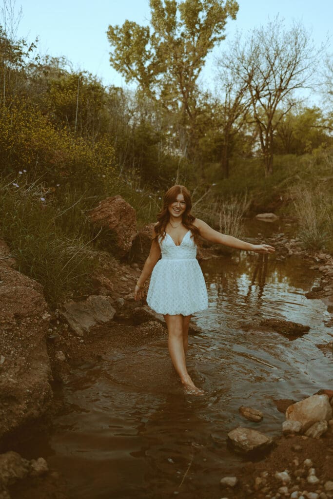 Senior wearing a neutral outfit that photograph beautifully during a golden hour spring senior photo session in a creek in Abilene, TX
