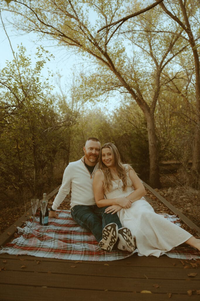 Couple wearing neutral outfits that photograph beautifully during a golden hour fall couples photo session on a wooded bridge in Abilene, TX