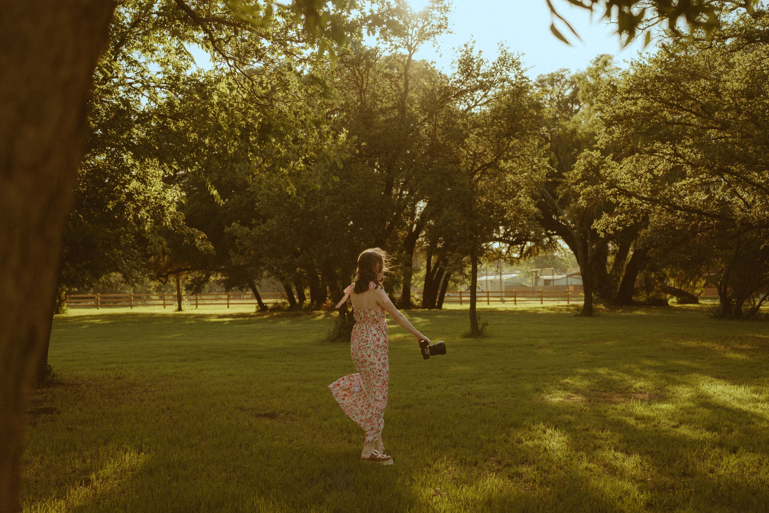 Abilene photographer Morgan Rose walking through a sunlit field holding her camera, showcasing the heart behind her nostalgic photography brand and creative business.