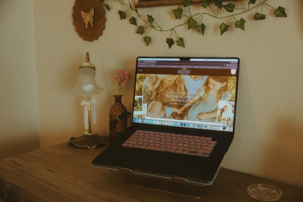 Cozy home office workspace featuring a laptop displaying a Showit photography website, surrounded by vintage butterfly artwork, ivy garland, and warm decor, illustrating website design and branding for photographers comparing Showit vs Pixieset.