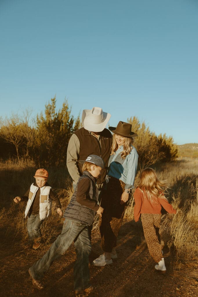Family walking together on a dirt path during golden hour in West Texas while children run and play around their parents. A candid lifestyle family photography moment with warm light, movement, and nostalgic storytelling by Morgan Rose Photography.