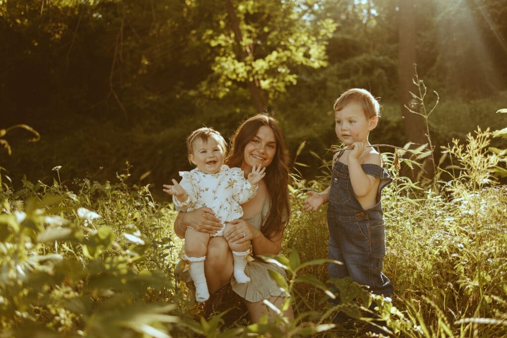 Mother holding her two young children in a sunlit open field during golden hour in Abilene, Texas. A warm and nostalgic motherhood photography session captured with natural light and candid emotion by Morgan Rose Photography.