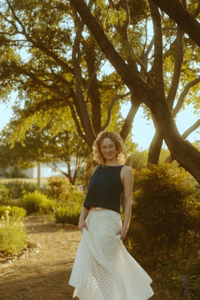 High school senior photographed during a golden hour summer photo session in Abilene, Texas with warm evening light, natural greenery, and breathable summer clothing.