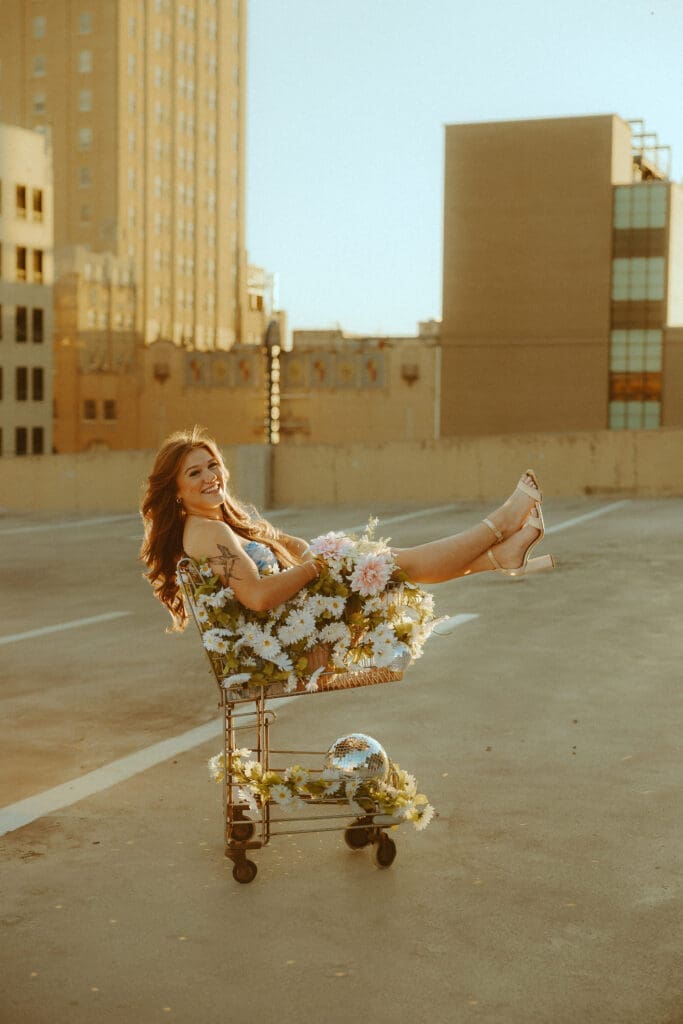 Senior portrait photographed during golden hour on a downtown rooftop in Abilene, Texas, featuring warm sunlight, soft glow, and creative storytelling photography with flowers and disco balls.