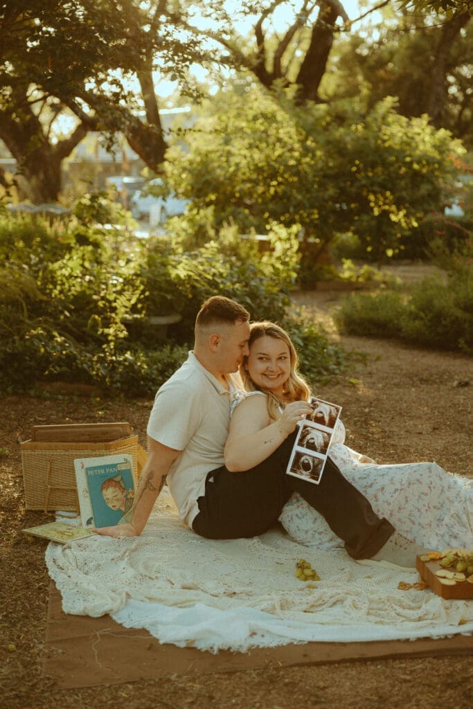 Expecting couple sitting together during a golden hour maternity announcement session in Abilene, Texas, holding ultrasound photos while surrounded by warm natural light and a cozy picnic setup.