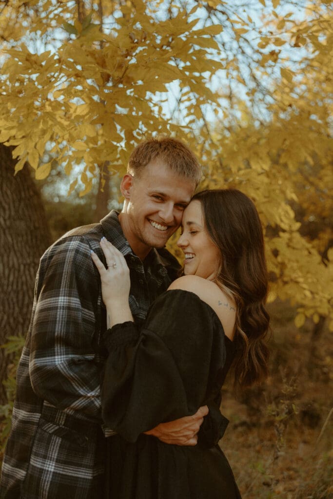 Couple sharing a joyful embrace beneath golden autumn trees during a golden hour couples photography session in Abilene, Texas.
