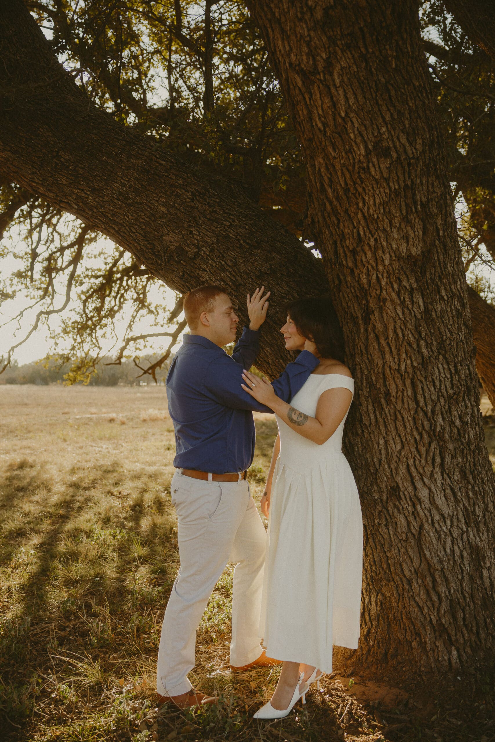 Couple sharing a quiet moment under a large tree during a golden hour photography session in Abilene, TX.