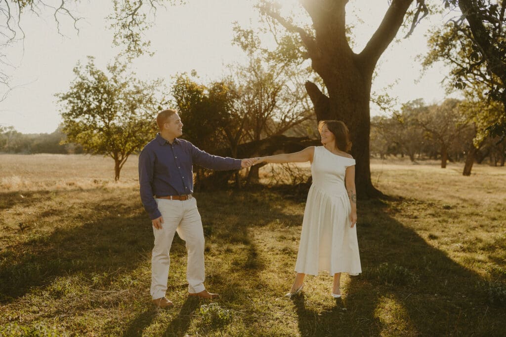Couple holding hands beneath a large tree during a golden hour couples photography session in Abilene, TX.