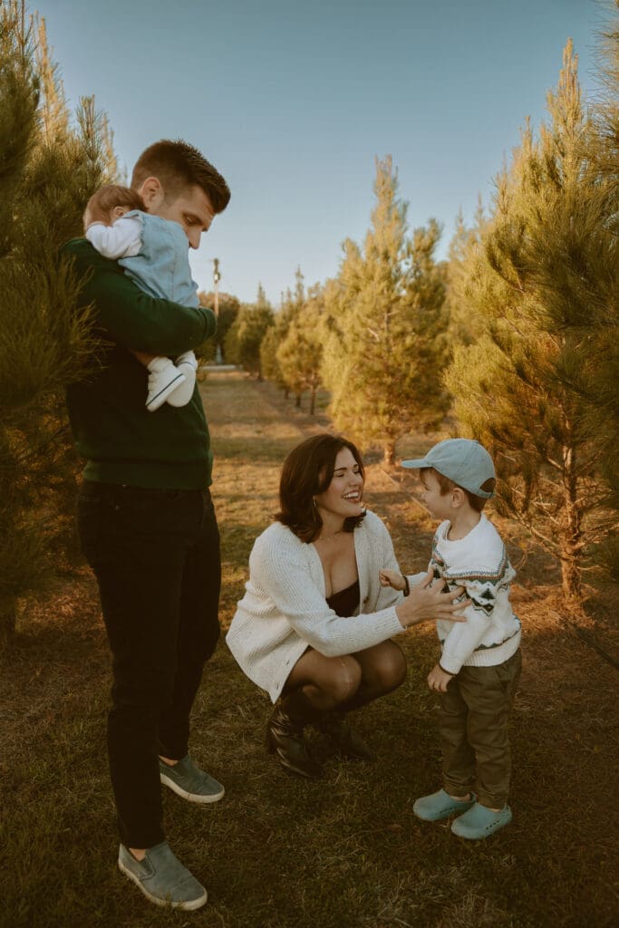 A father cradles his baby while a mother smiles and kneels to talk with her young son during a golden hour family photography session in Abilene, Texas, capturing an everyday moment of love and connection.