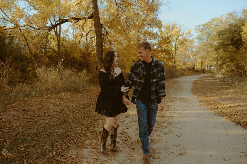 Couple walking together during a fall photography session surrounded by golden trees in Abilene, Texas.