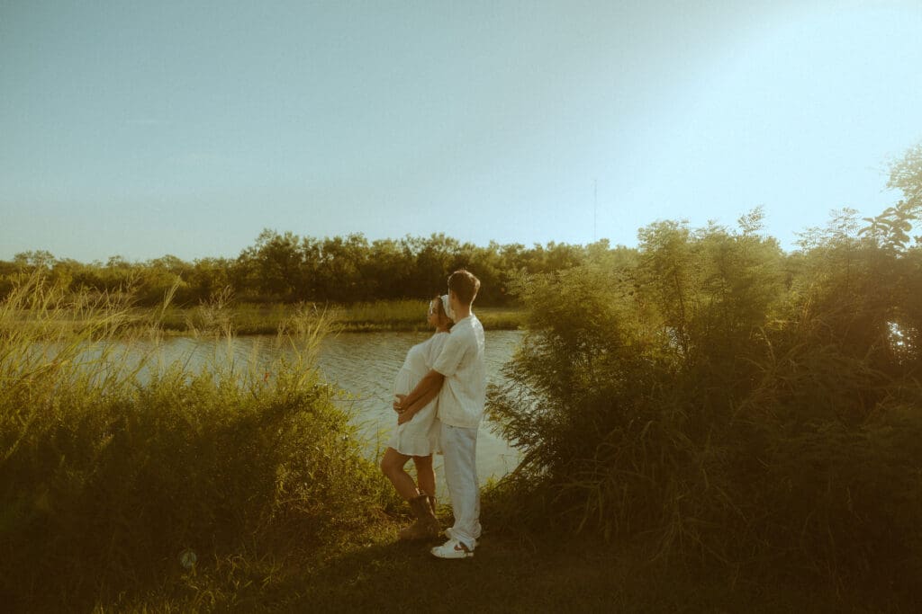 Expecting couple embracing by the water during a golden hour maternity session in Abilene, Texas, showing a natural maternity pose.