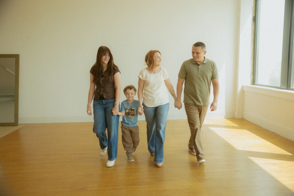 Family of four walking hand in hand and sharing smiles during a candid lifestyle family photography session in a sunlit studio in Abilene, Texas.