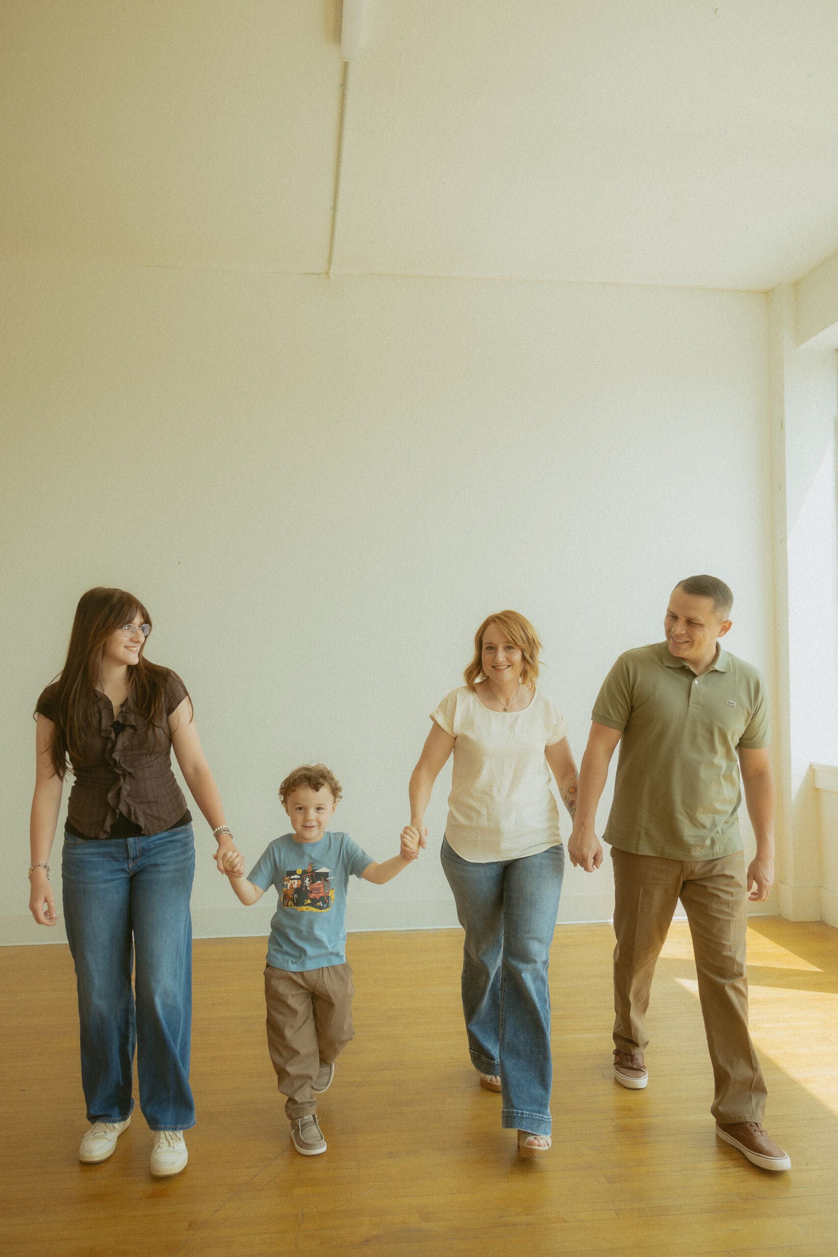 Family of four holding hands and walking together during a lifestyle family photography session in a naturally lit studio in Abilene, Texas.