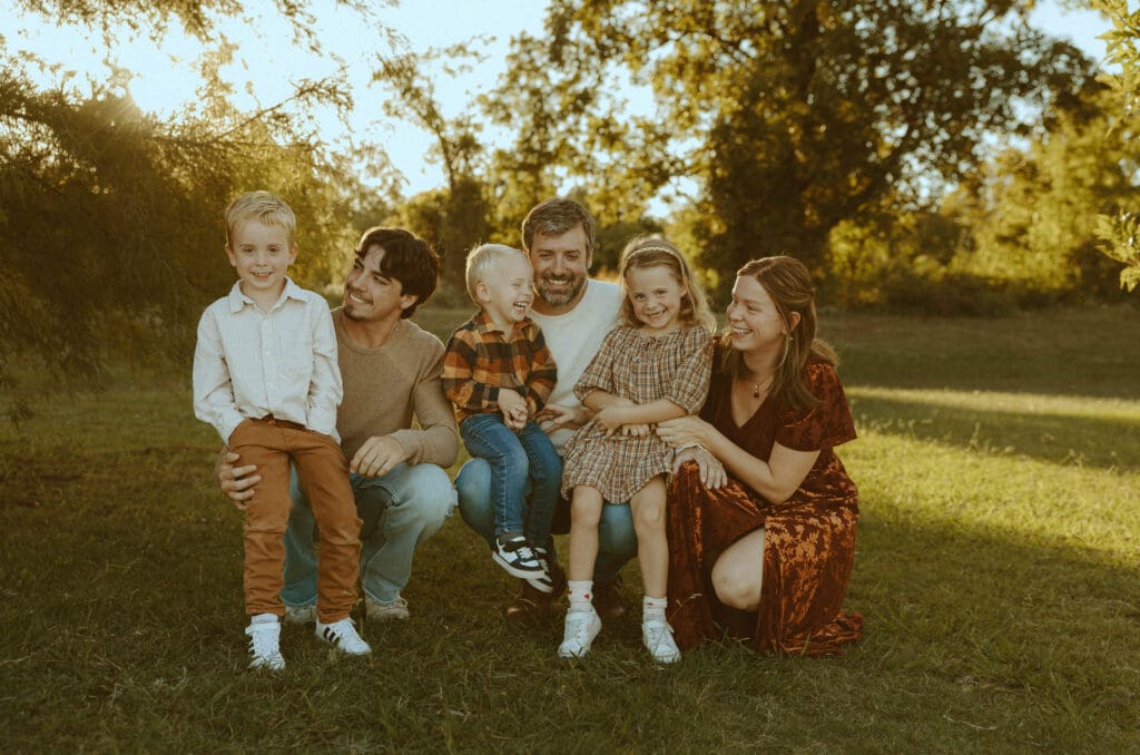 Family laughing together in cozy, coordinated fall outfits during a golden hour photo session in Abilene, Texas.